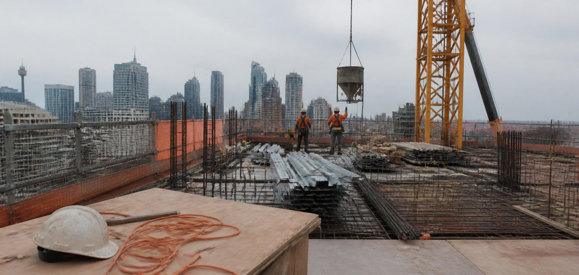 High-rise construction deck in Sydney — reinforcement bar, formwork and a yellow tower crane lifting a concrete bucket, workers in hi-vis and harnesses on the slab edge — Spire Safety WHS consultants Sydney